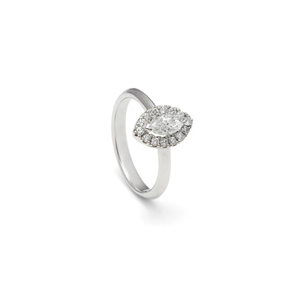 Anillo de compromiso con frente ovalado. Una orla de pequeñas piedras perfila el centro del diseño.