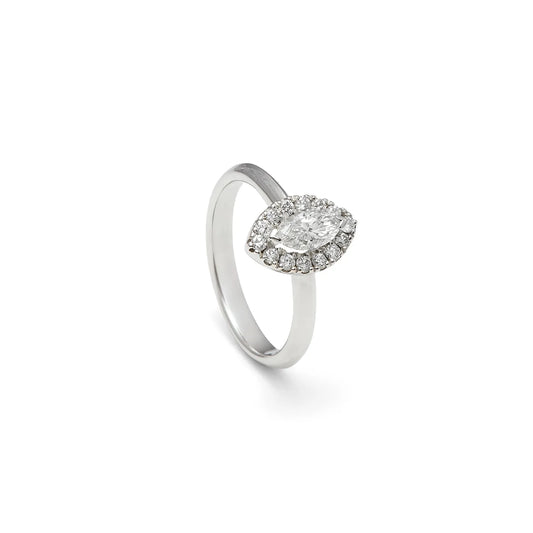 Anillo de compromiso con frente ovalado. Una orla de pequeñas piedras perfila el centro del diseño.