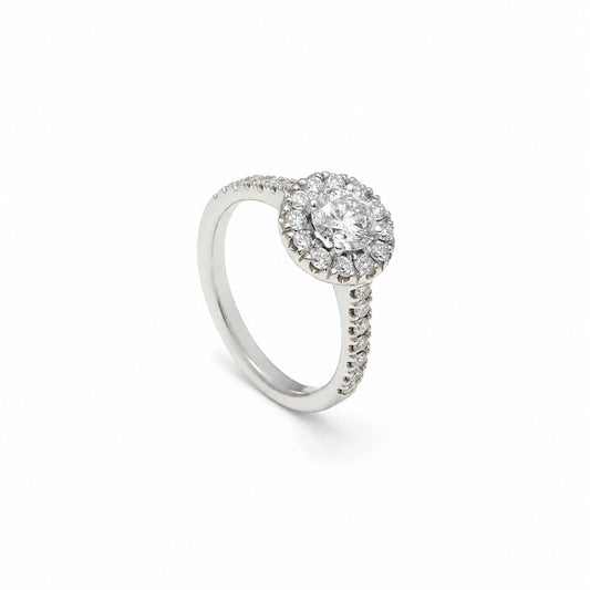 Anillo rosetón con aro luminoso. Una orla de pequeñas piedras perfila el centro incoloro.