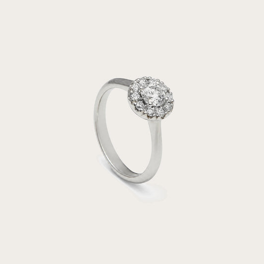 Anillo rosetón de aro liso. El centro incoloro queda rodeado por pequeñas piedras luminosas.