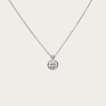 Colgante solitario de círculo luminoso. Un borde fino de tono plateado perfila la piedra incolora.