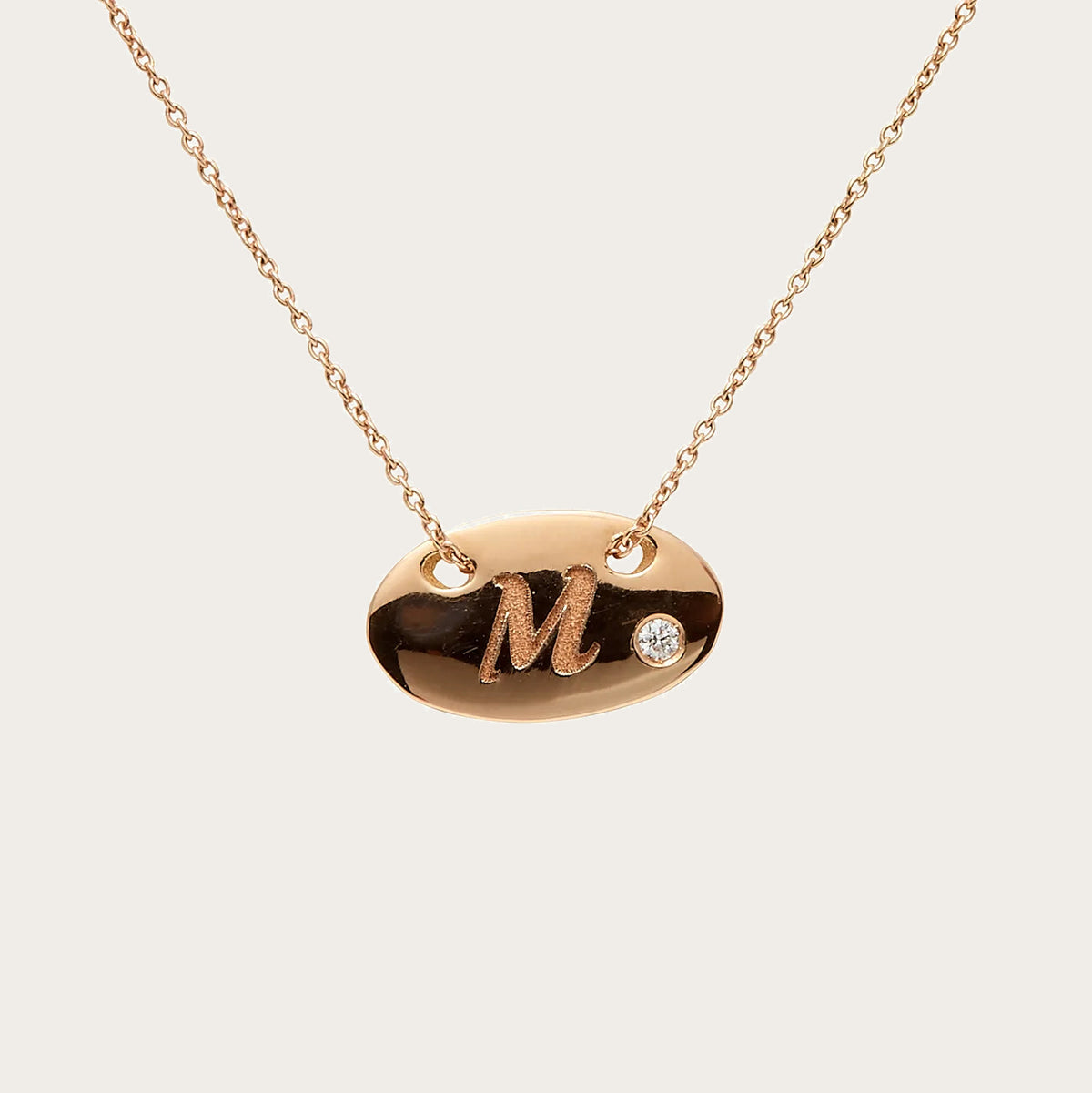Colgante oval de inicial. La letra M destaca sobre la superficie lisa del motivo.