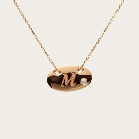 Colgante oval de inicial. La letra M destaca sobre la superficie lisa del motivo.