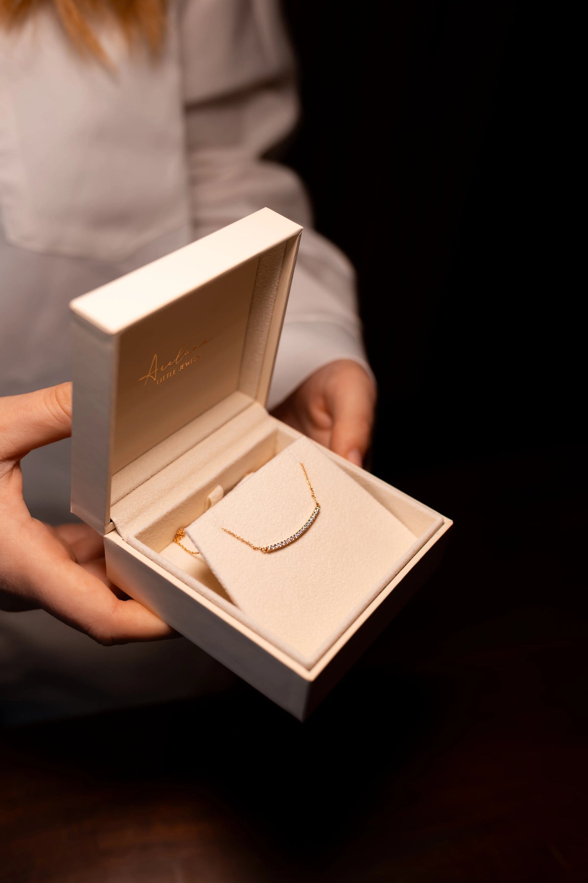 Colgante de barra curva de diamantes en su estuche de Arelana, sostenido entre las manos