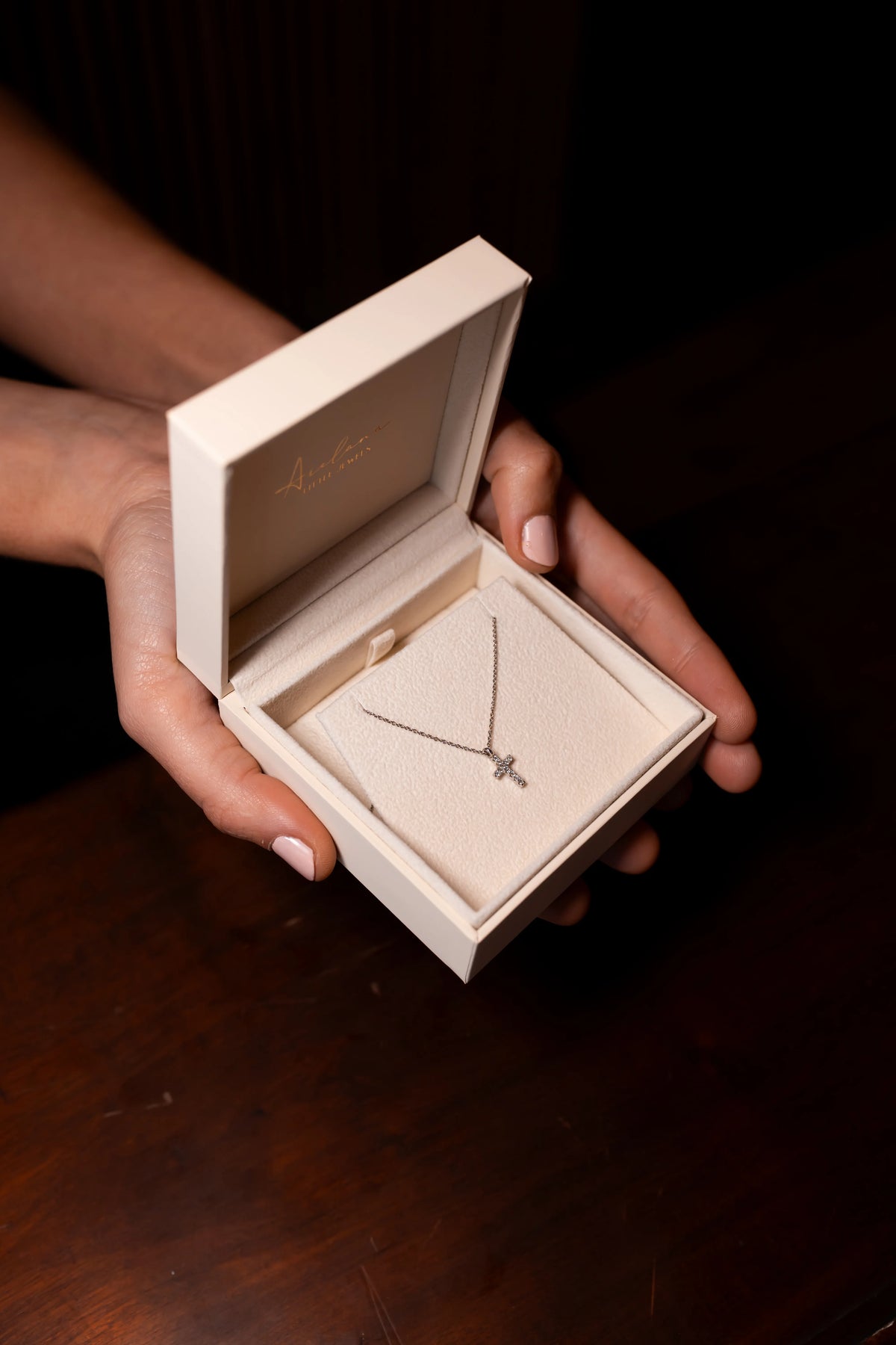 Colgante de cruz de diamantes en su estuche de Arelana, sostenido entre las manos