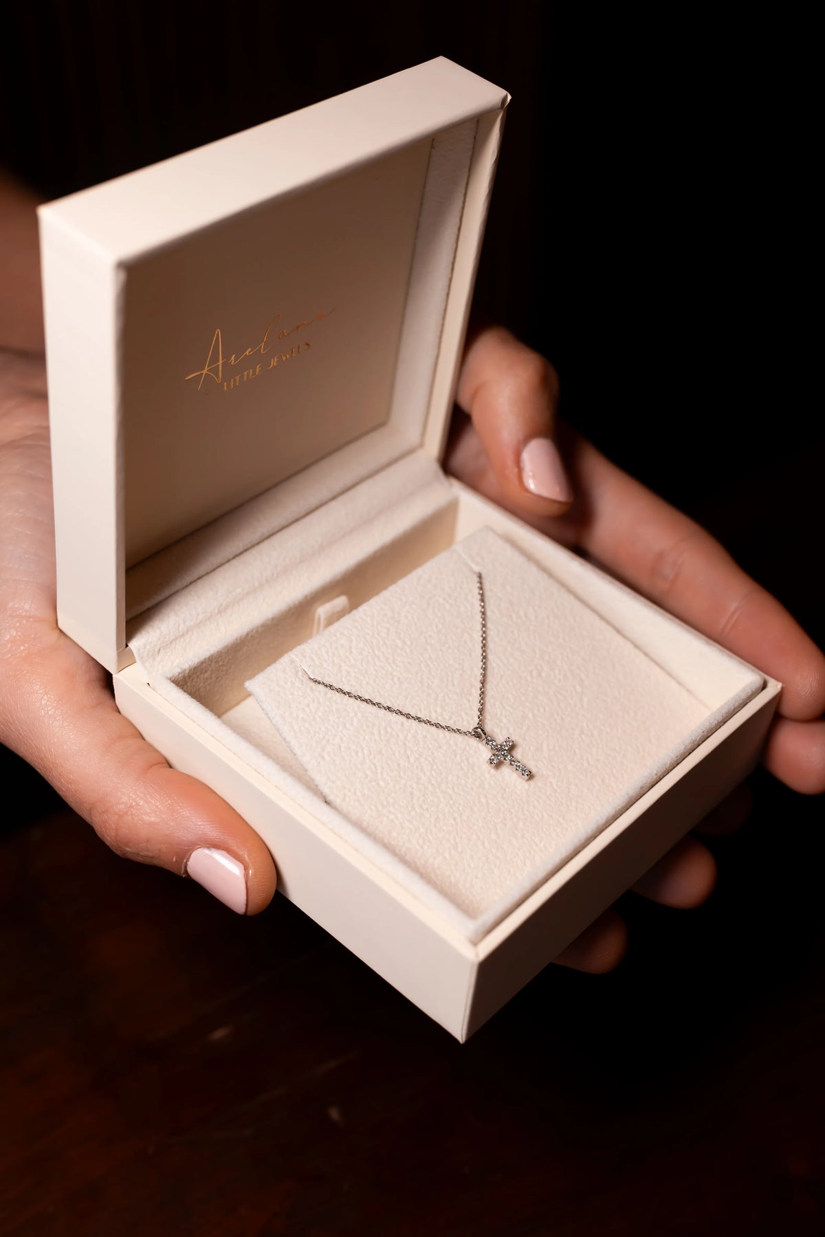 Estuche de Arelana abierto con el colgante de cruz de diamantes sobre el acolchado