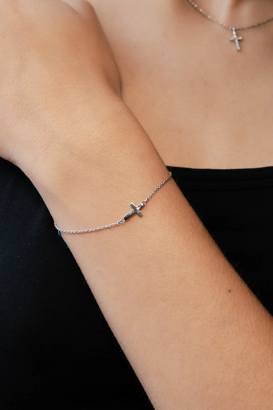 Pulsera de cadena fina de oro blanco con cruz de diamantes, puesta en la muñeca y con colgante a juego