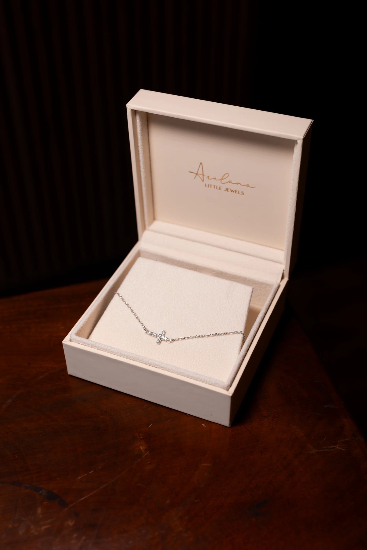Pulsera de cruz de diamantes en su estuche de Arelana sobre una mesa de madera