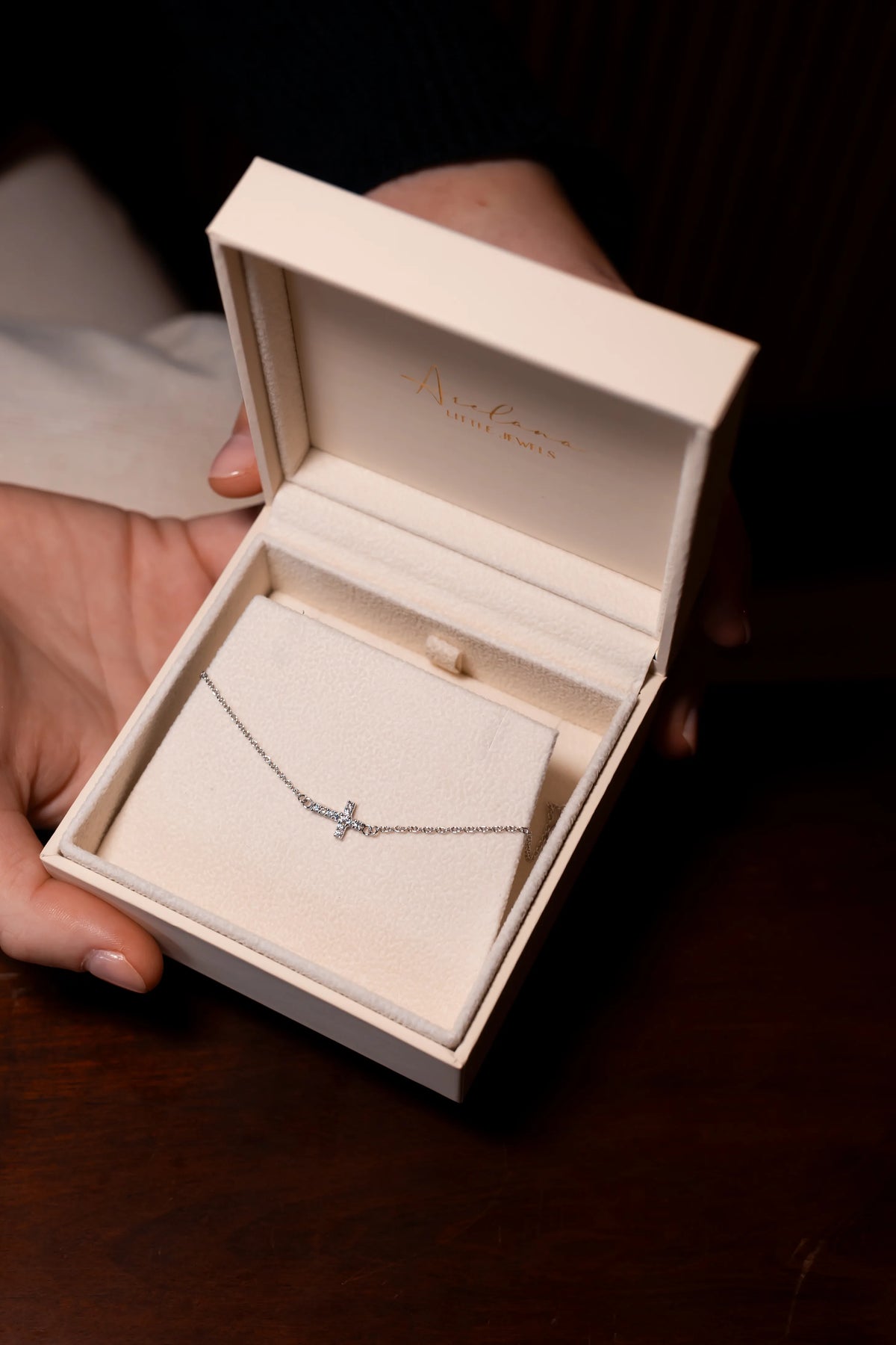 Estuche de Arelana abierto entre las manos con la pulsera de cruz de diamantes